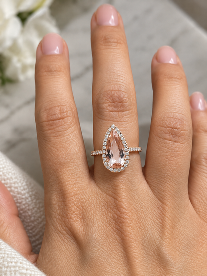 Pear shaped morganite ring in 18K rose gold with a 2.58 carat pink gemstone, round diamond halo and pavé diamond band.