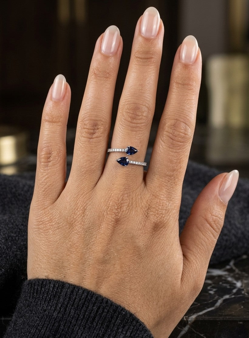 18K white gold blue sapphire Toi et Moi ring featuring two pear-shaped blue sapphires positioned in opposite directions with round diamonds along the open band.