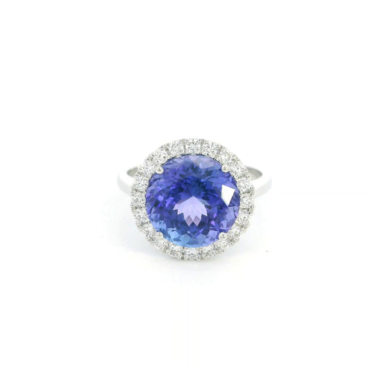 Round tanzanite and diamond halo ring in 18K white gold featuring a 5.97 carat violet-blue tanzanite surrounded by round diamonds on a polished band.