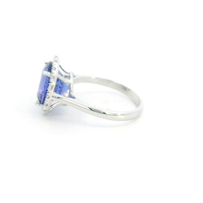 Round tanzanite and diamond halo ring in 18K white gold featuring a 5.97 carat violet-blue tanzanite surrounded by round diamonds on a polished band.