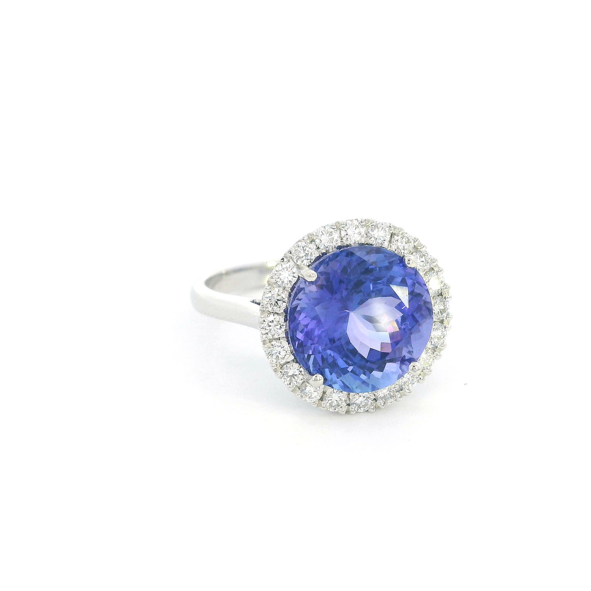 Round tanzanite and diamond halo ring in 18K white gold featuring a 5.97 carat violet-blue tanzanite surrounded by round diamonds on a polished band.
