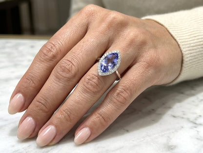 Marquise tanzanite and diamond halo ring in 18K white gold featuring a blue-violet gemstone surrounded by round diamonds.