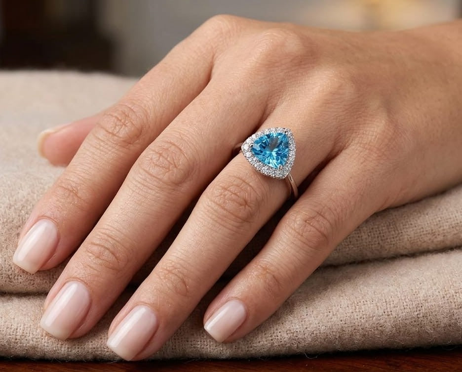 18K white gold ring with a triangular bright blue topaz surrounded by round diamonds and polished split-shank shoulders.