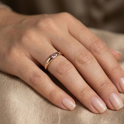 Pink tourmaline ring in 18K rose gold featuring a small round pink gemstone set into a smooth, polished, rounded gold band.