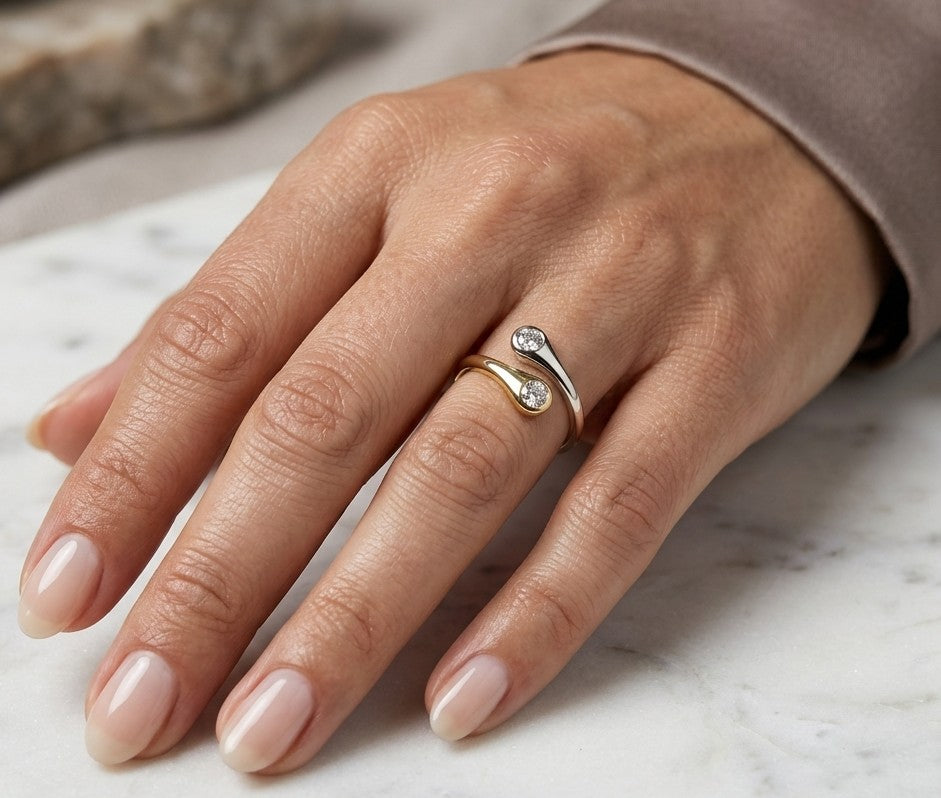 18K white and yellow gold bypass ring with two round diamonds in bezel settings at the ends of curved, overlapping bands.