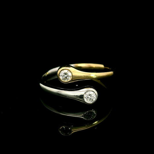 18K white and yellow gold bypass ring with two round diamonds in bezel settings at the ends of curved, overlapping bands.