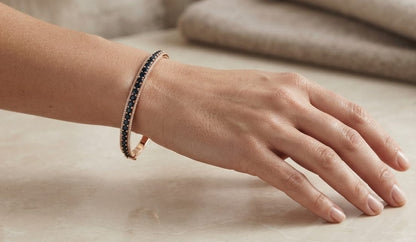 18K rose gold bangle featuring a row of round blue sapphires framed by two rows of round diamonds