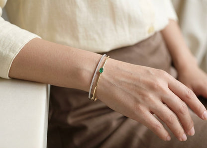 18K yellow gold open bangle with oval green emerald and a row of round brilliant diamonds