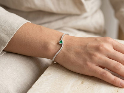 18K white gold diamond bangle with heart-shaped green emerald, diamond halo and sweeping round diamond rows