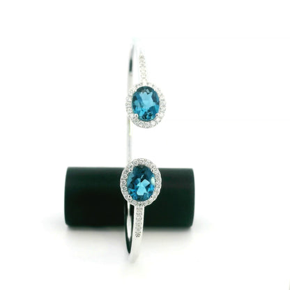 18K white gold open cuff bangle featuring two oval natural London Blue Topaz gemstones totaling 4.21 carats, surrounded by natural diamond halos totaling 0.57 carat.