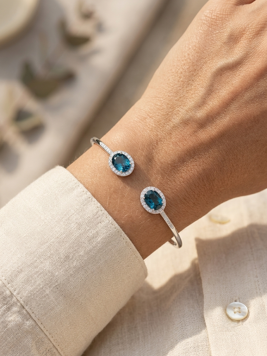 18K white gold open cuff bangle featuring two oval natural London Blue Topaz gemstones totaling 4.21 carats, surrounded by natural diamond halos totaling 0.57 carat.