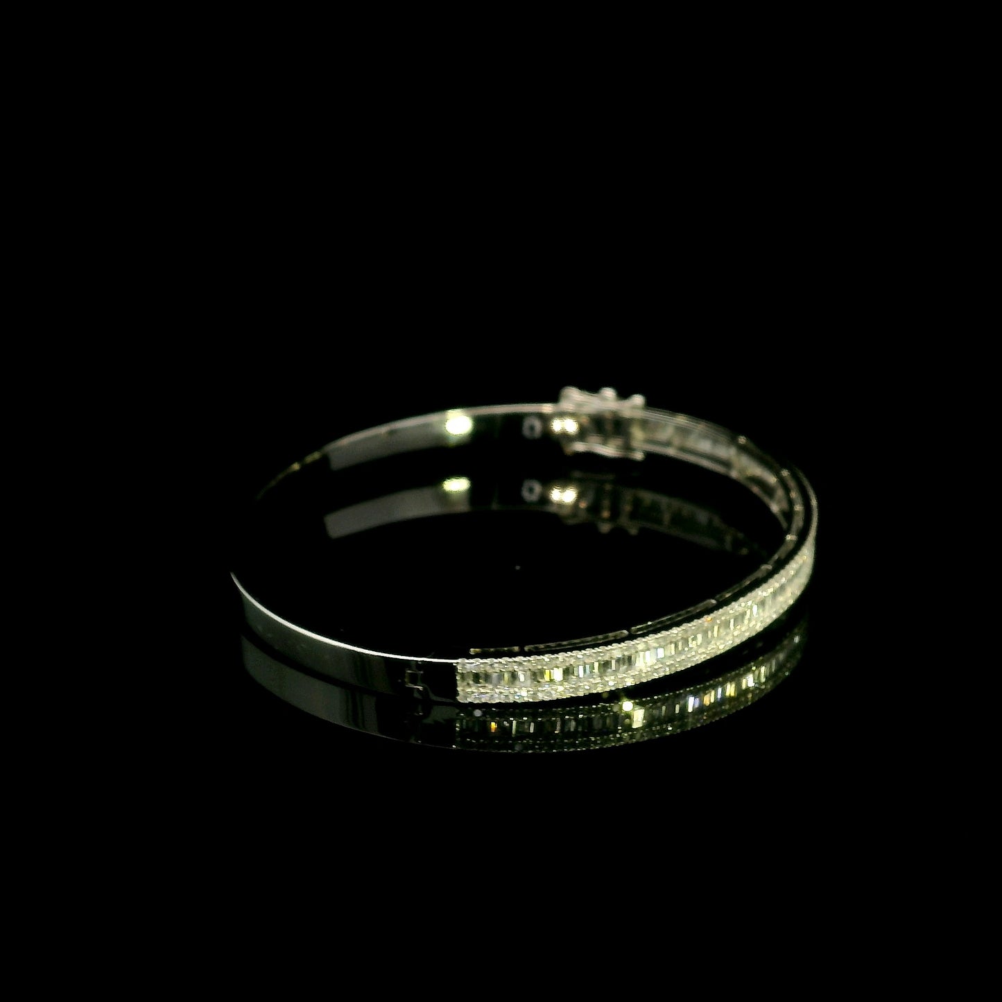 18K white gold diamond bangle with a central row of baguette diamonds framed by round brilliant diamonds and secure hinged clasp