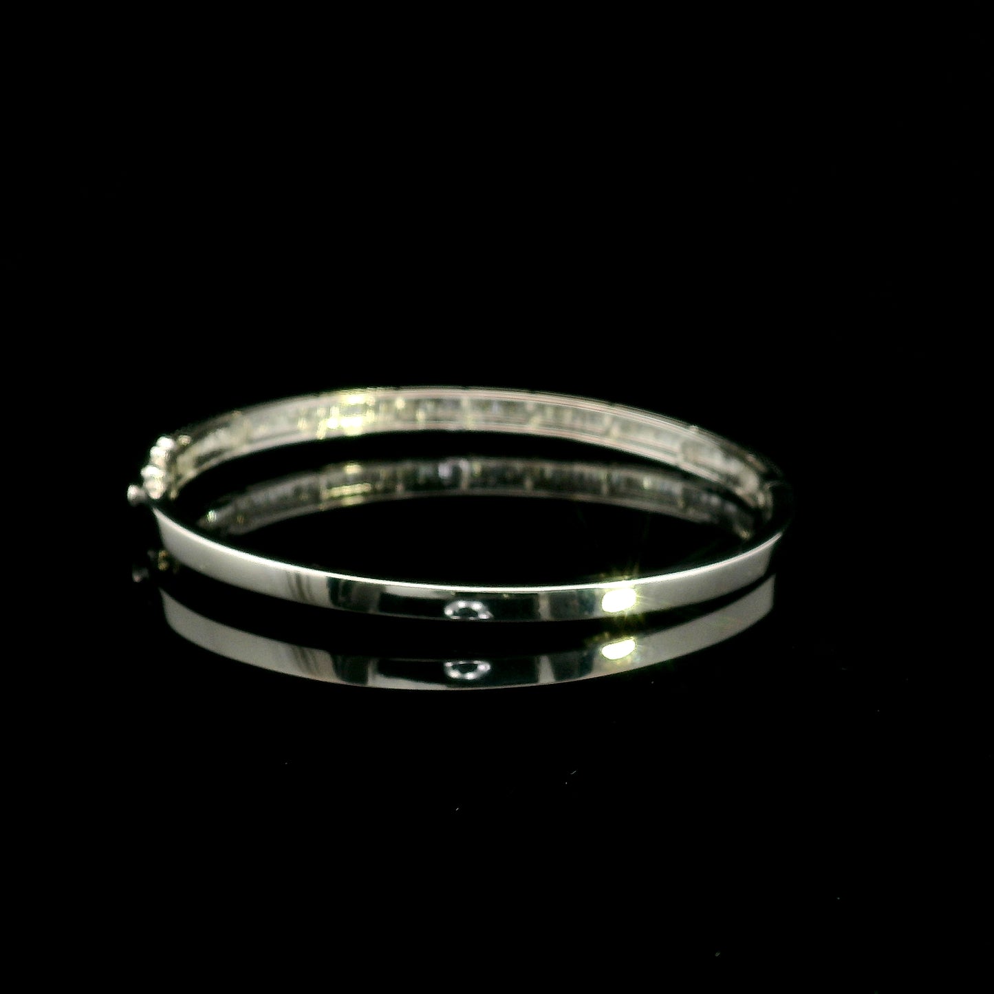 18K white gold diamond bangle with a central row of baguette diamonds framed by round brilliant diamonds and secure hinged clasp