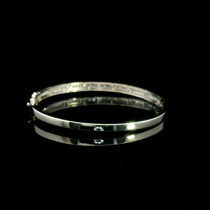 18K white gold diamond bangle with a central row of baguette diamonds framed by round brilliant diamonds and secure hinged clasp