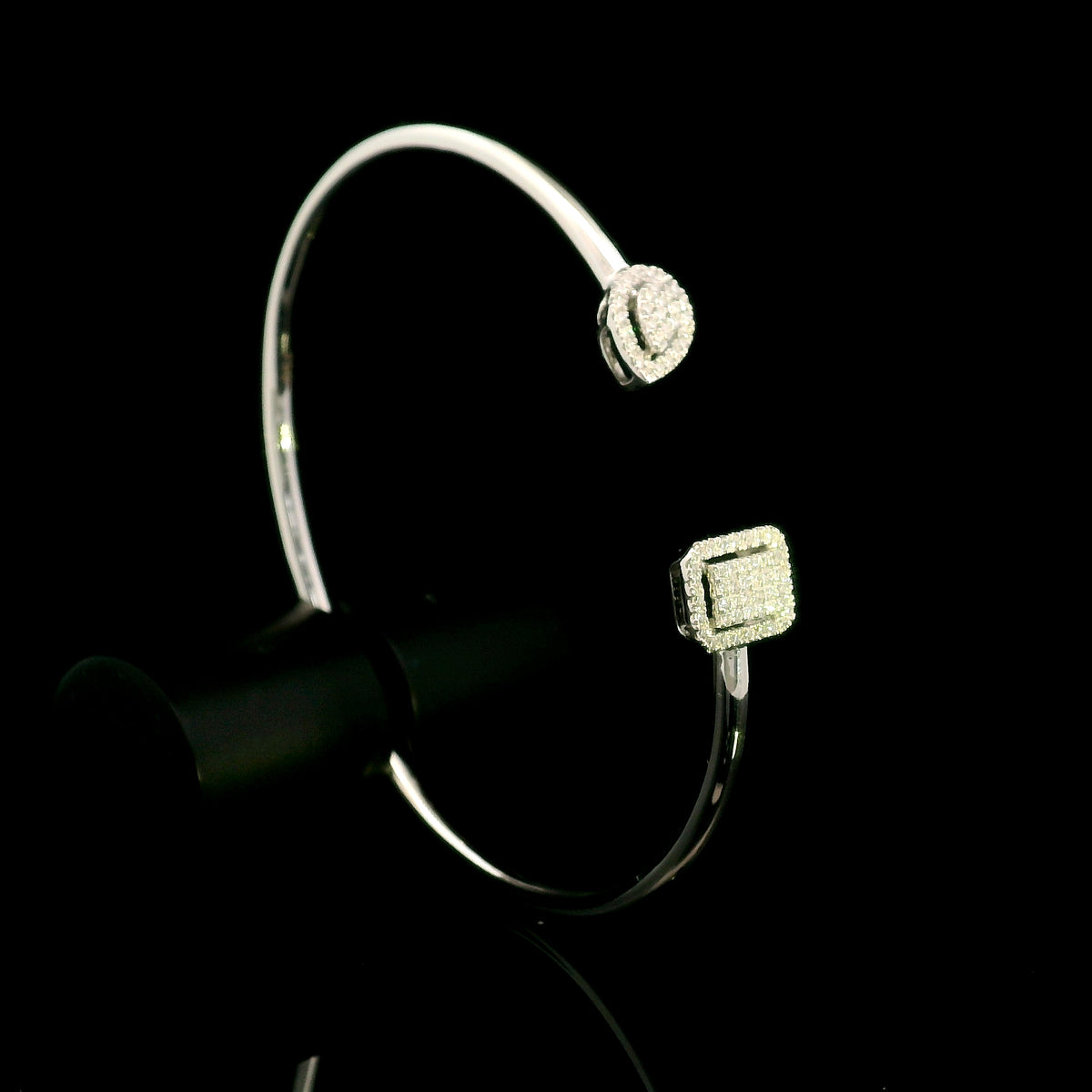 Geometric diamond open bangle in 18K white gold with contrasting pear-shaped and rectangular diamond motifs.
