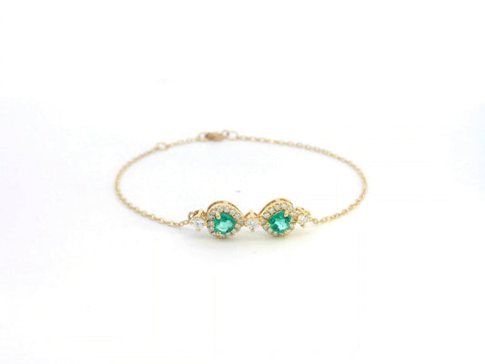 18K gold bracelet featuring two heart-shaped emeralds (0.57ct) with diamond halos (0.38ct) on a delicate chain.