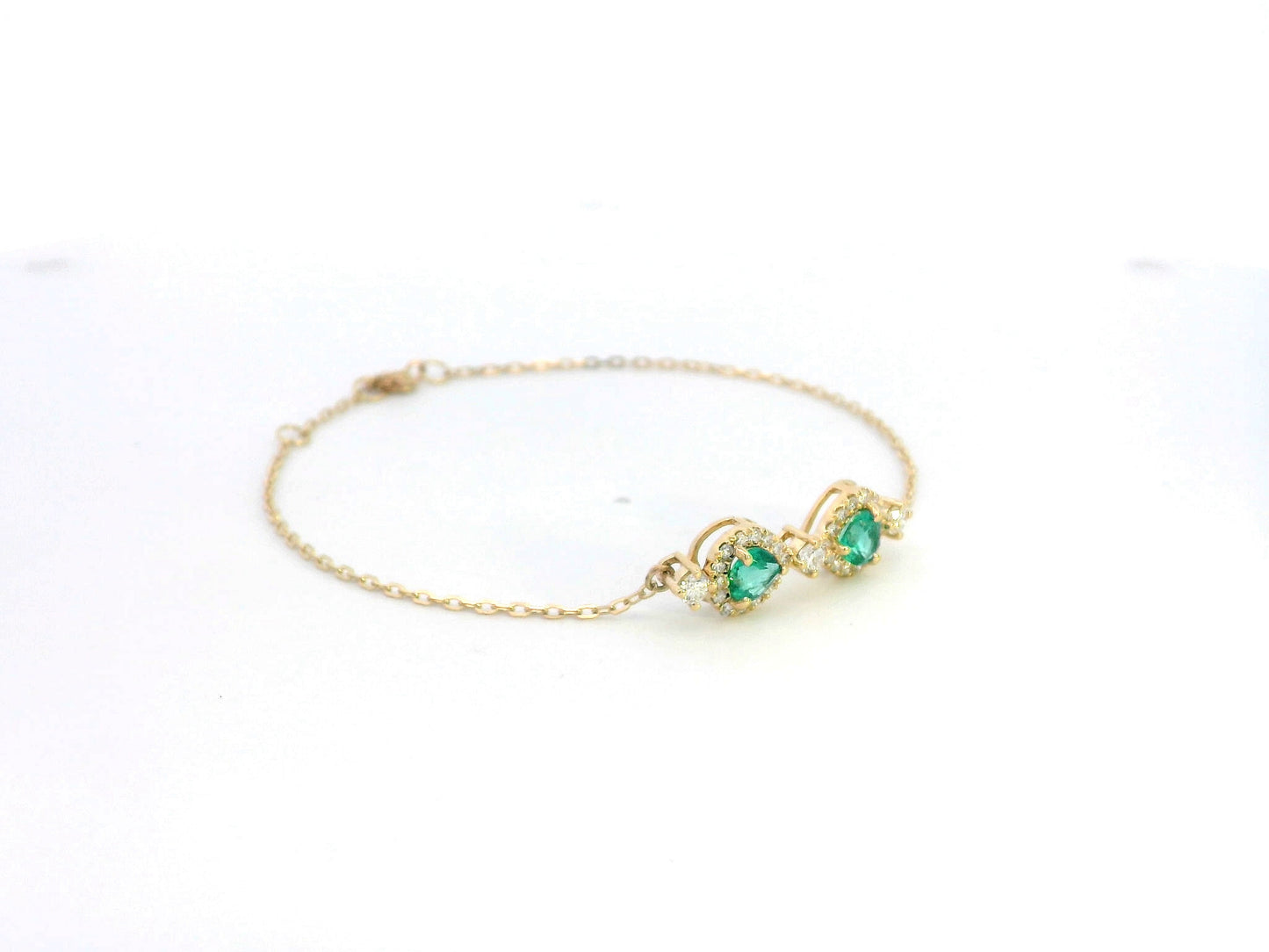 18K gold bracelet featuring two heart-shaped emeralds (0.57ct) with diamond halos (0.38ct) on a delicate chain.