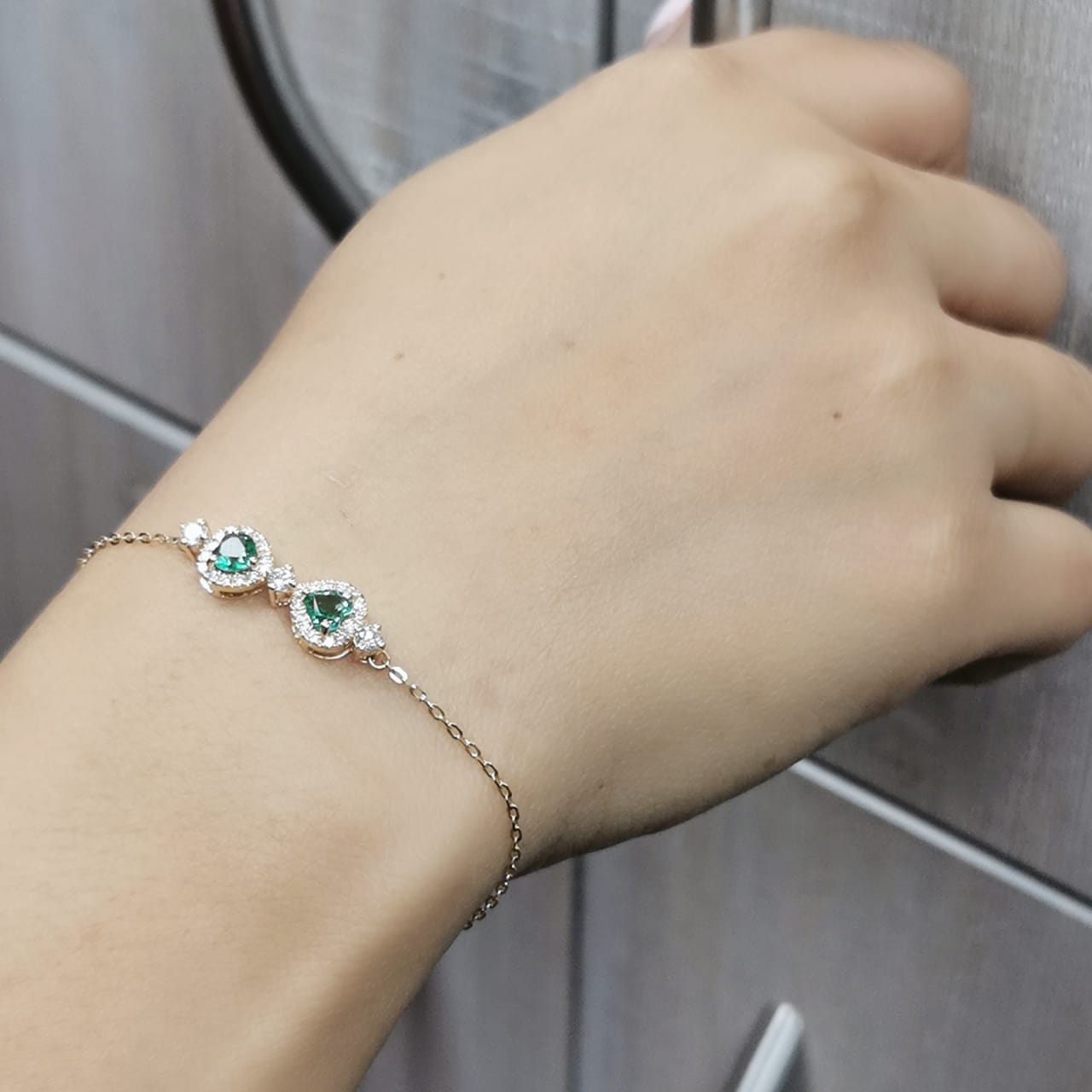 18K gold bracelet featuring two heart-shaped emeralds totaling 0.57 carats, surrounded by a sparkling 0.38 carat diamond halo, set on a delicate gold chain for a timeless and romantic jewelry piece.