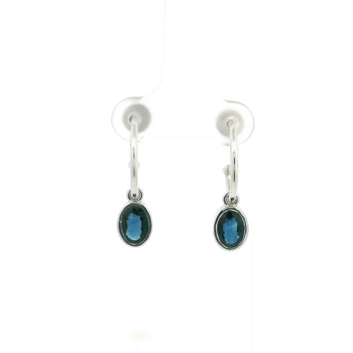 Oval blue sapphire drop hoop earrings in 18K white gold with polished hoops and suspended sapphire drops.