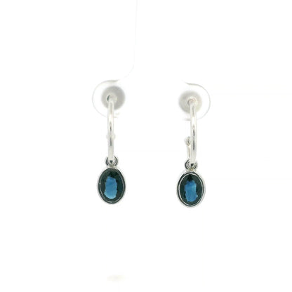Oval blue sapphire drop hoop earrings in 18K white gold with polished hoops and suspended sapphire drops.