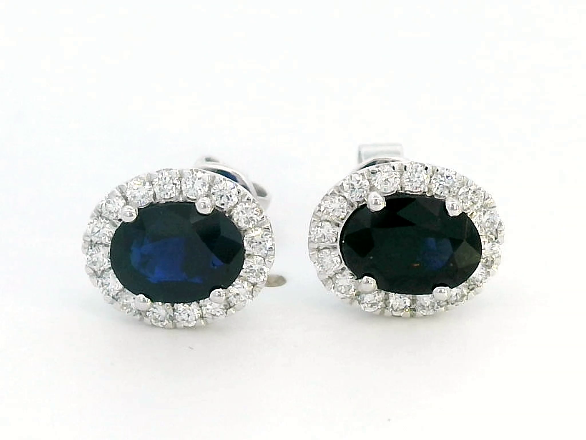 18K gold stud earrings featuring 1.88 carat oval blue sapphires and a 0.33 carat diamond halo, perfect for September birthstone jewelry.