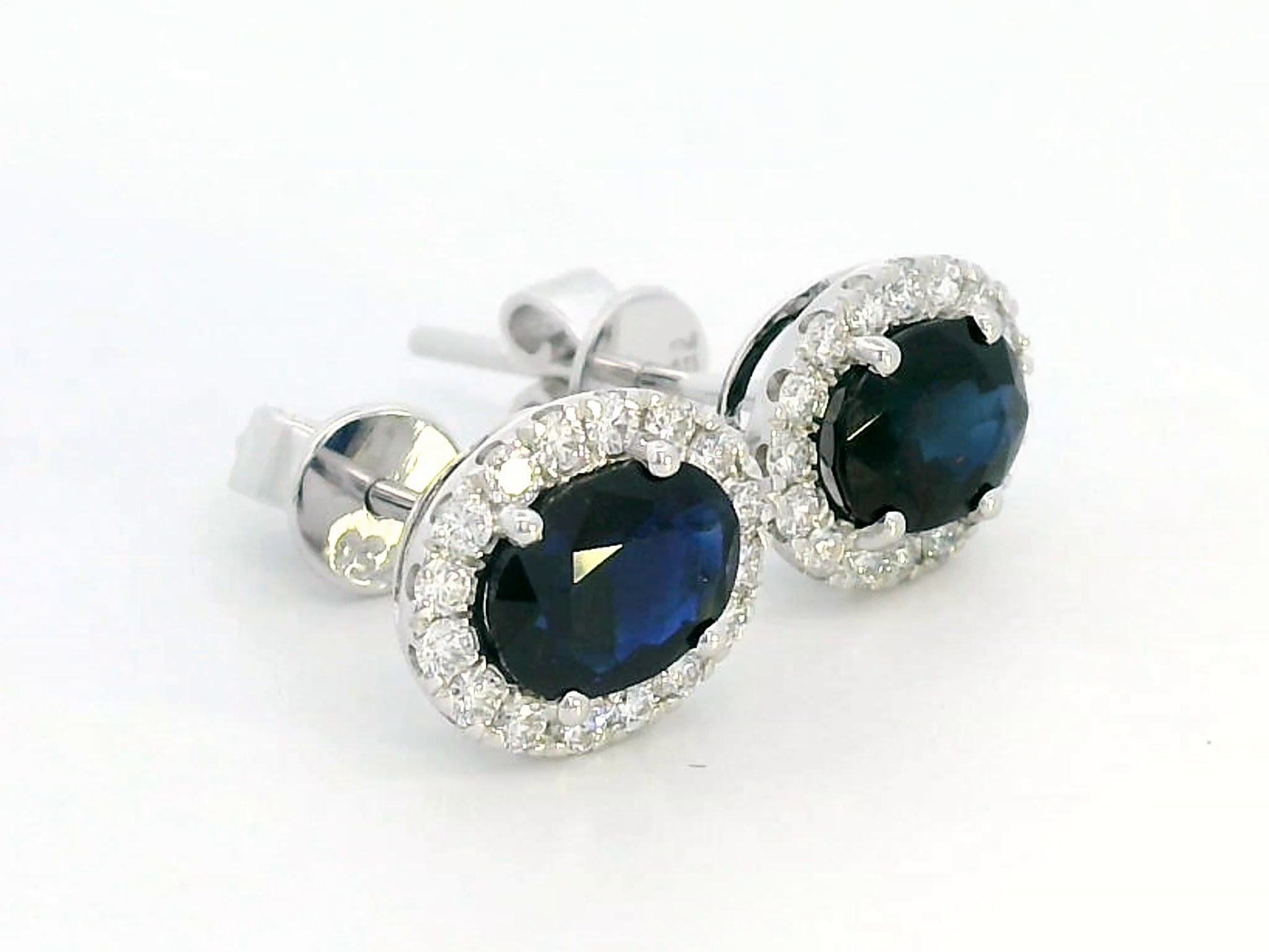 18K gold stud earrings featuring 1.88 carat oval blue sapphires and a 0.33 carat diamond halo, perfect for September birthstone jewelry.