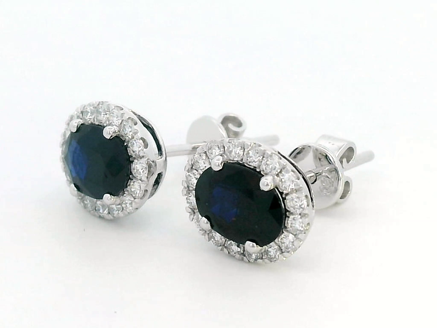 18K gold stud earrings featuring 1.88 carat oval blue sapphires and a 0.33 carat diamond halo, perfect for September birthstone jewelry.