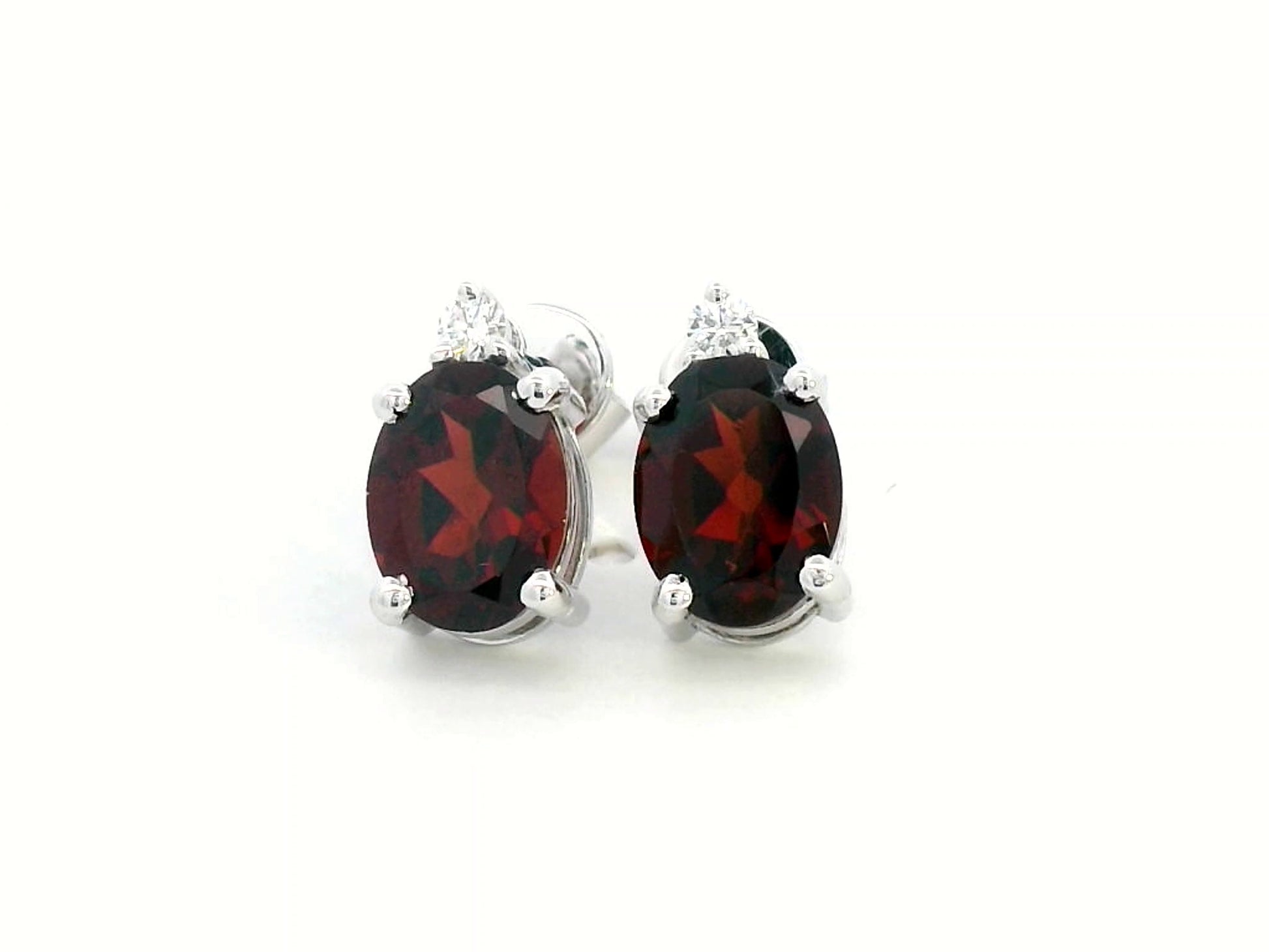 18K white gold garnet and diamond stud earrings featuring oval-cut 3.09-carat garnets with 0.07-carat diamond accents, set in a classic four-prong setting with push-back closures.