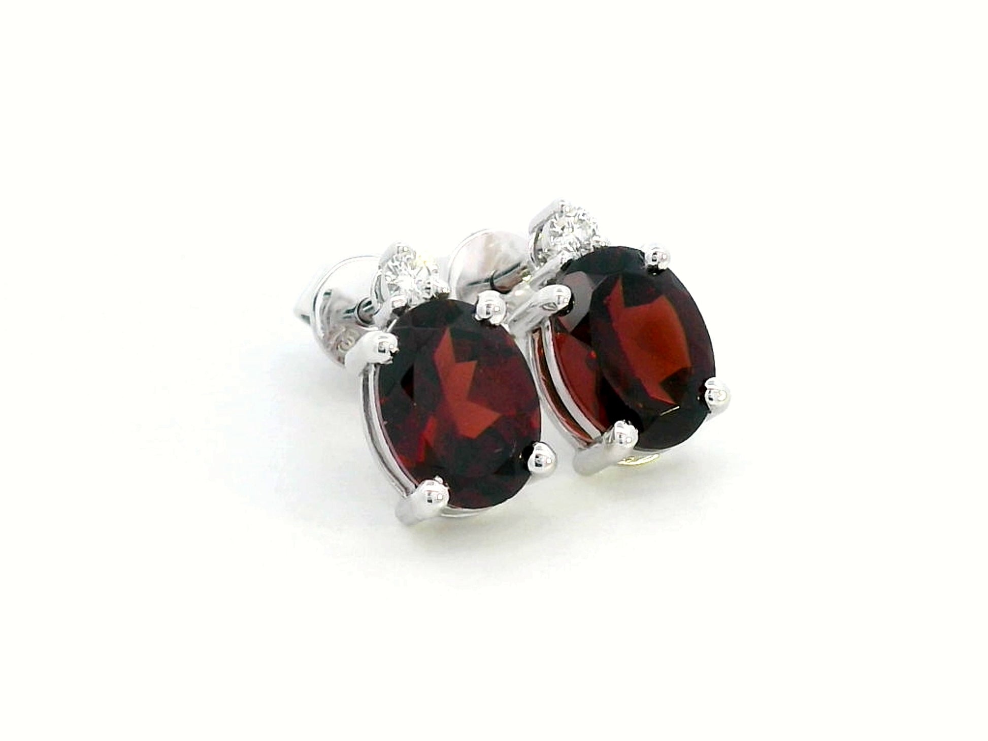 18K white gold garnet and diamond stud earrings featuring oval-cut 3.09-carat garnets with 0.07-carat diamond accents, set in a classic four-prong setting with push-back closures.