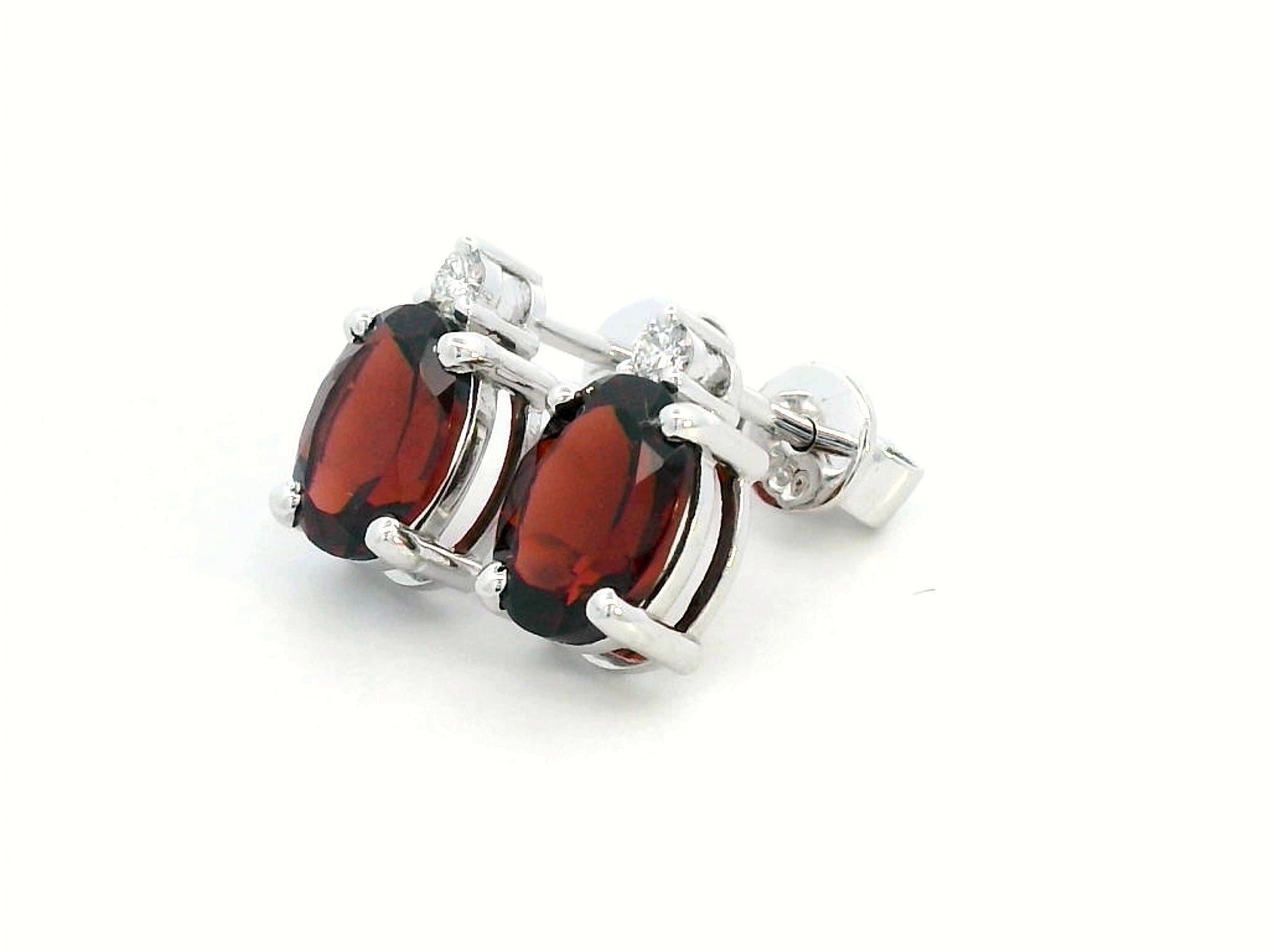 18K white gold garnet and diamond stud earrings featuring oval-cut 3.09-carat garnets with 0.07-carat diamond accents, set in a classic four-prong setting with push-back closures.