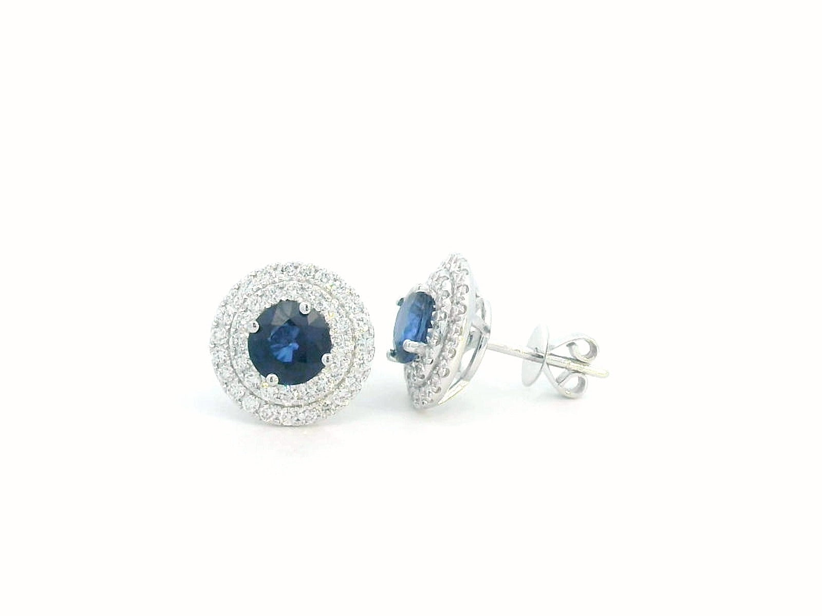 Round Sapphire and Diamond halo stud earrings in 18K white gold, featuring 2.27 carats of deep blue Sapphire and 0.81 carats of sparkling Diamonds.