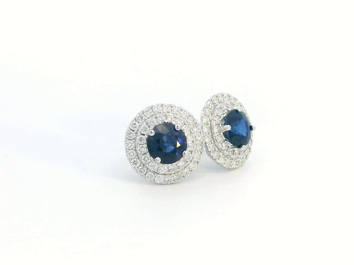 Round Sapphire and Diamond halo stud earrings in 18K white gold, featuring 2.27 carats of deep blue Sapphire and 0.81 carats of sparkling Diamonds.