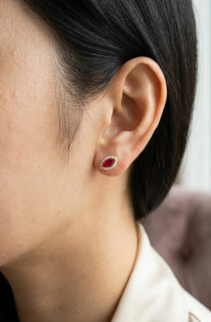 Marquise ruby and diamond halo stud earrings crafted in 18K yellow gold with natural rubies and round brilliant diamonds.