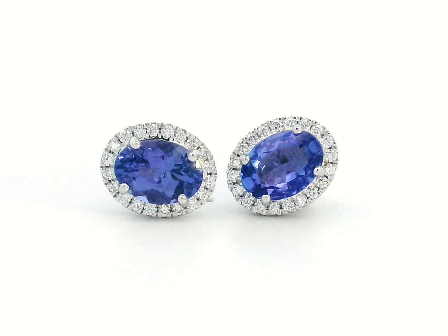 Elegant 18K white gold tanzanite and diamond halo earrings featuring 1.84ct oval tanzanites encircled by 0.19ct natural diamonds.