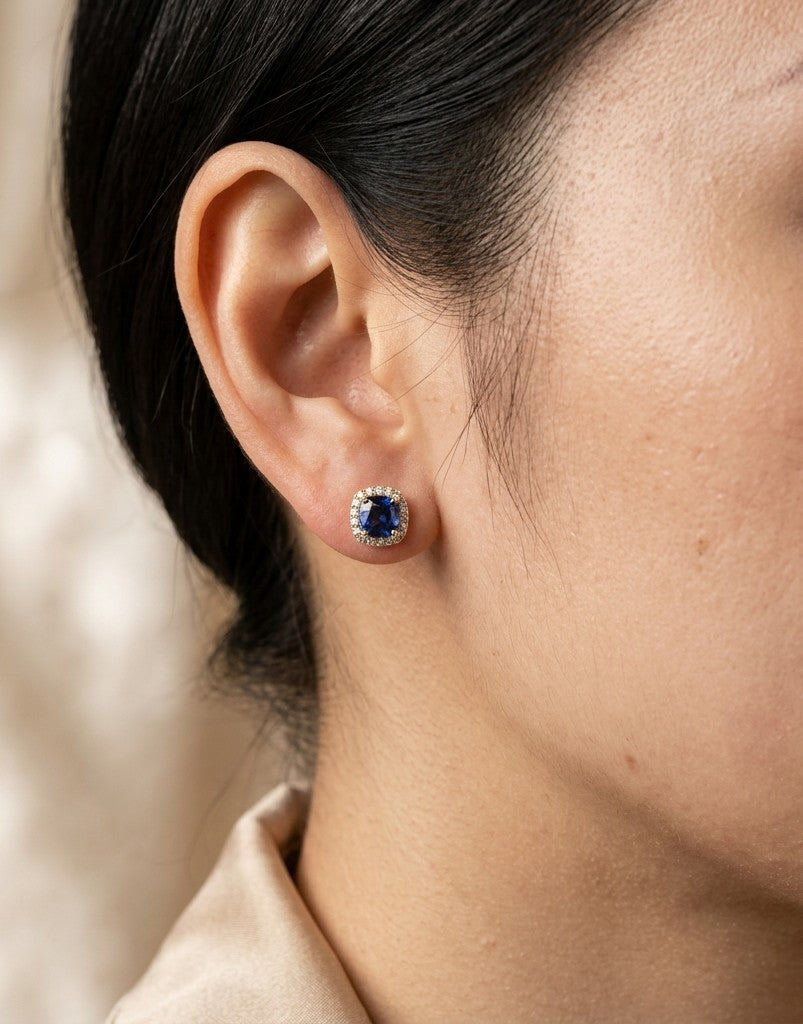 Cushion blue sapphire and diamond halo stud earrings in 18K yellow gold with natural sapphires surrounded by round brilliant diamonds.