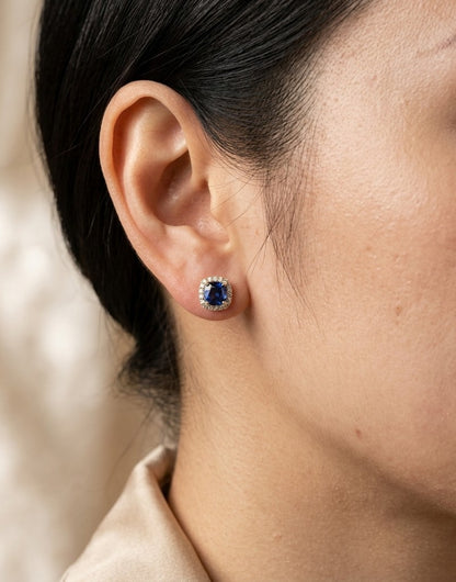 Cushion blue sapphire and diamond halo stud earrings in 18K yellow gold with natural sapphires surrounded by round brilliant diamonds.