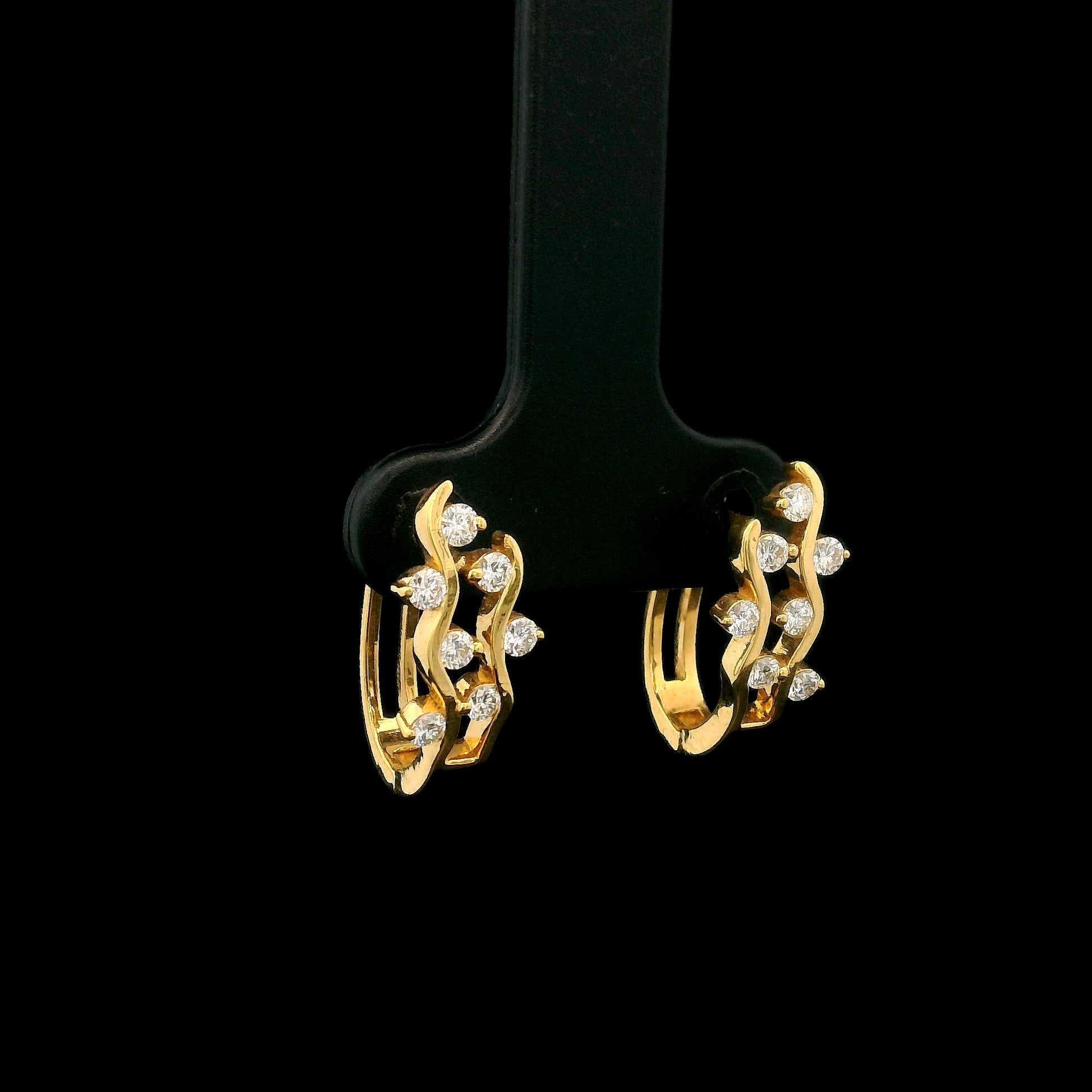 18K yellow gold diamond wave hoop earrings featuring flowing open gold curves with scattered round brilliant diamonds.