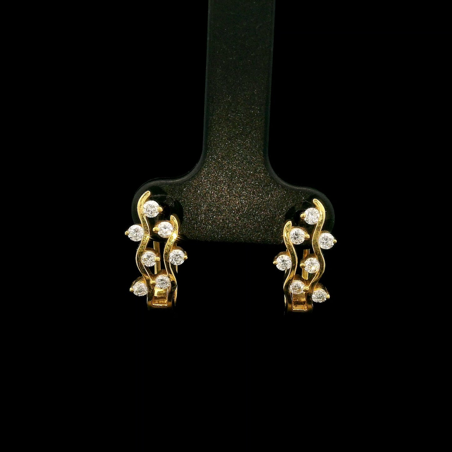 18K yellow gold diamond wave hoop earrings featuring flowing open gold curves with scattered round brilliant diamonds.