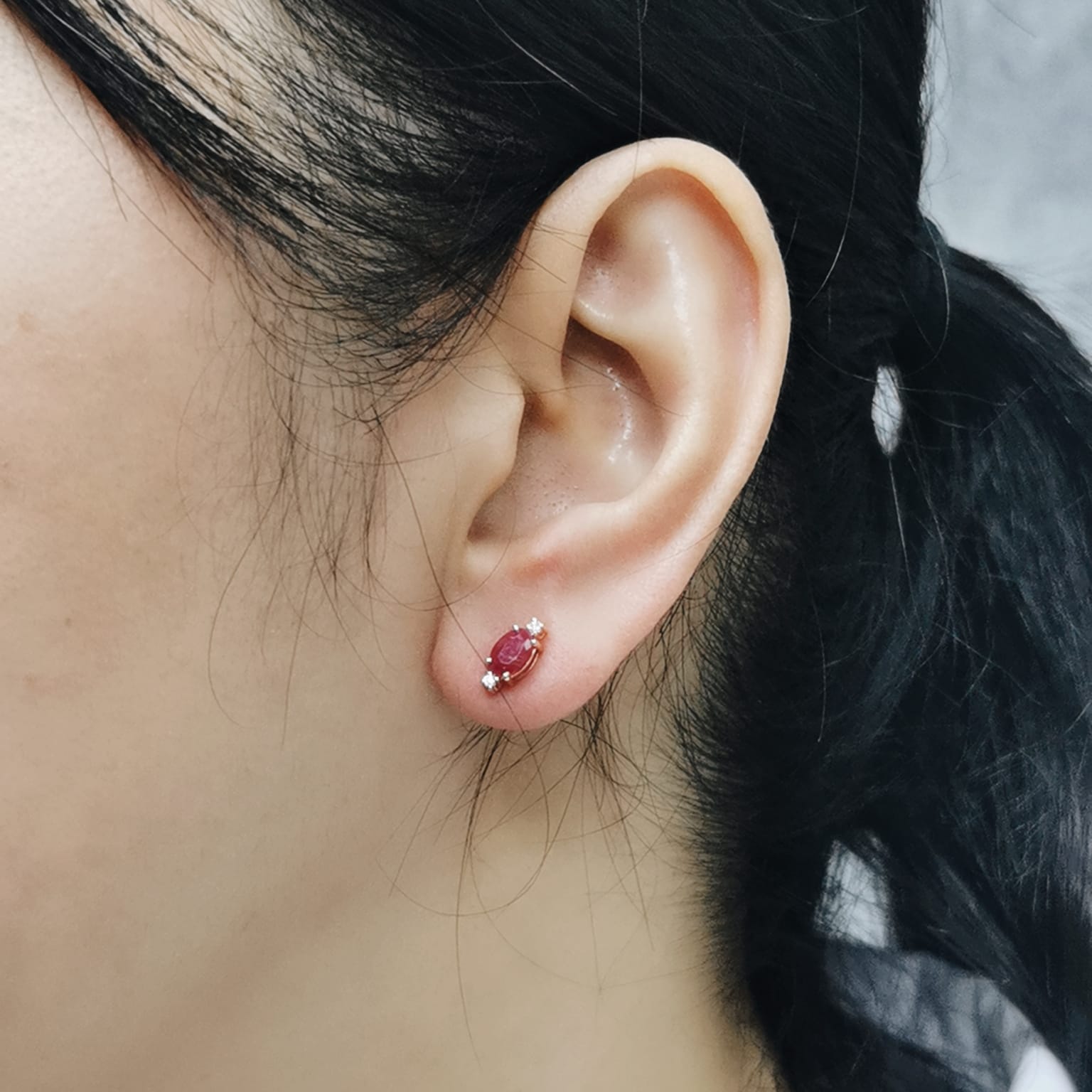 Close-up of an ear wearing a red gemstone earring with a blurred background
