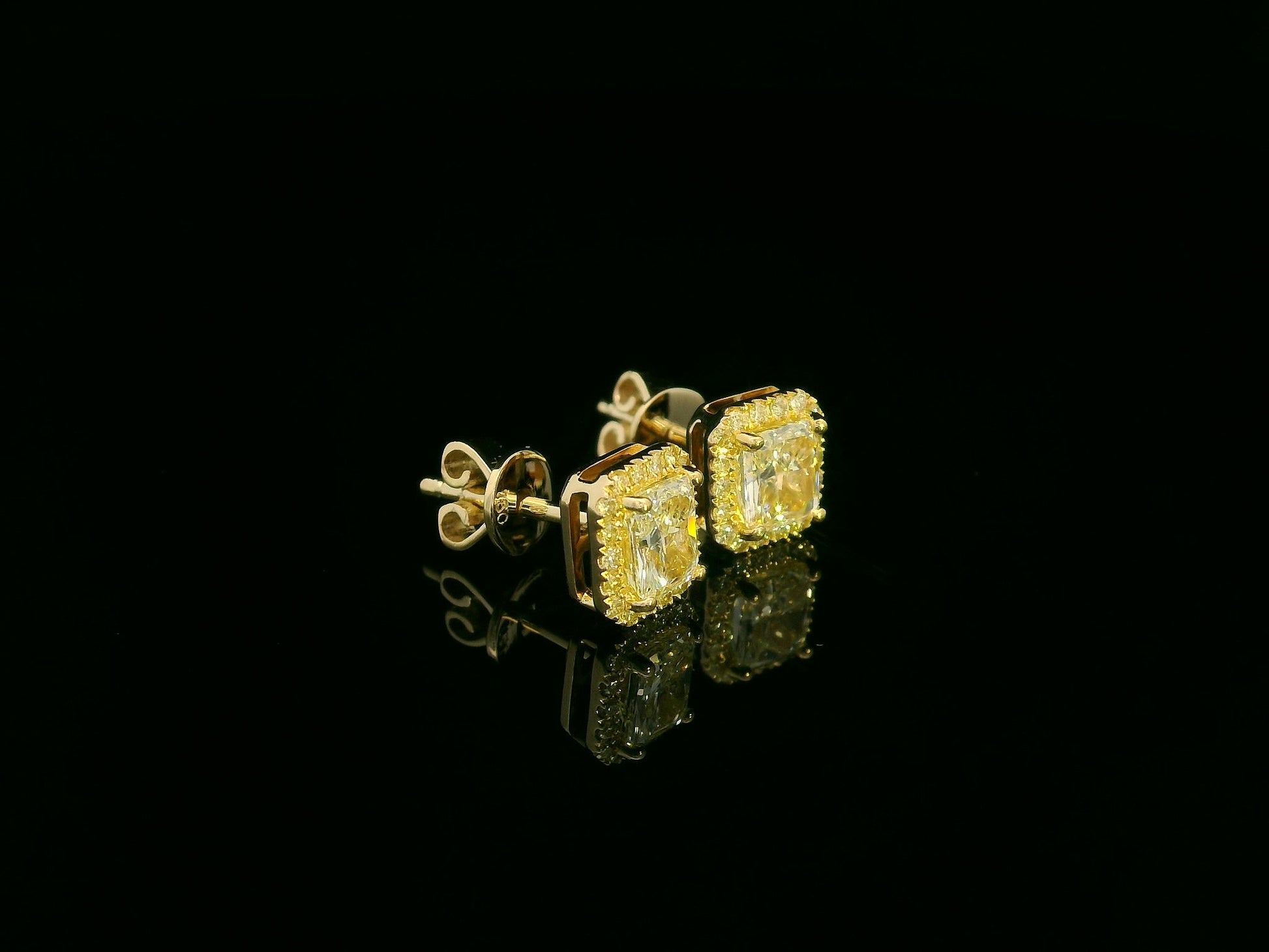 Side view of yellow gold earrings sparkling with radiant-cut fancy yellow diamonds