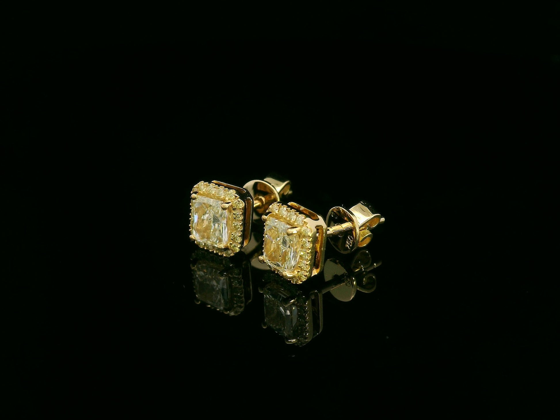 Side view of yellow gold earrings sparkling with radiant-cut fancy yellow diamonds
