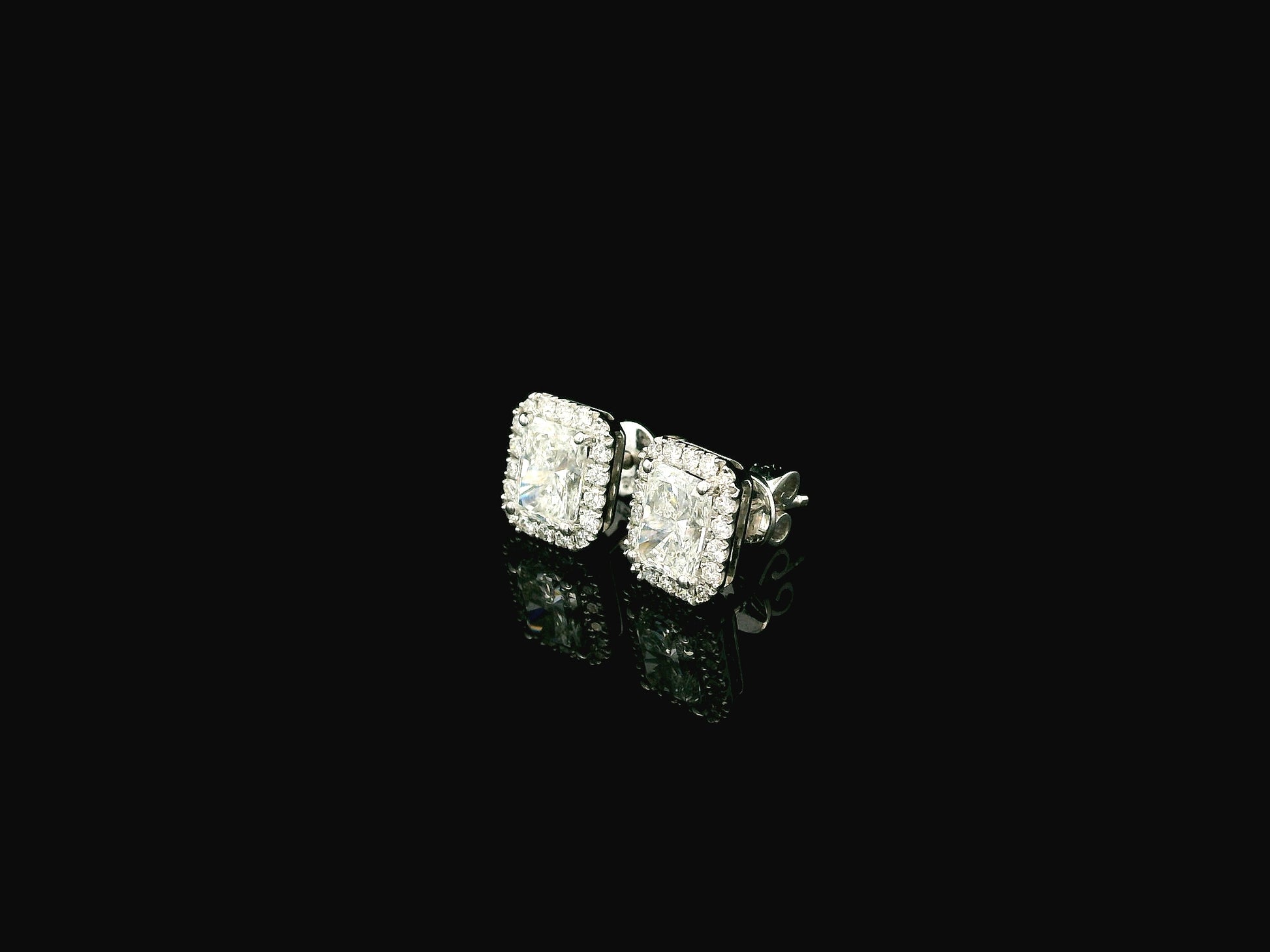 18K white gold diamond halo stud earrings featuring two GIA certified radiant cut diamonds totaling 1.40 carats surrounded by 0.27 carat natural diamond halos.