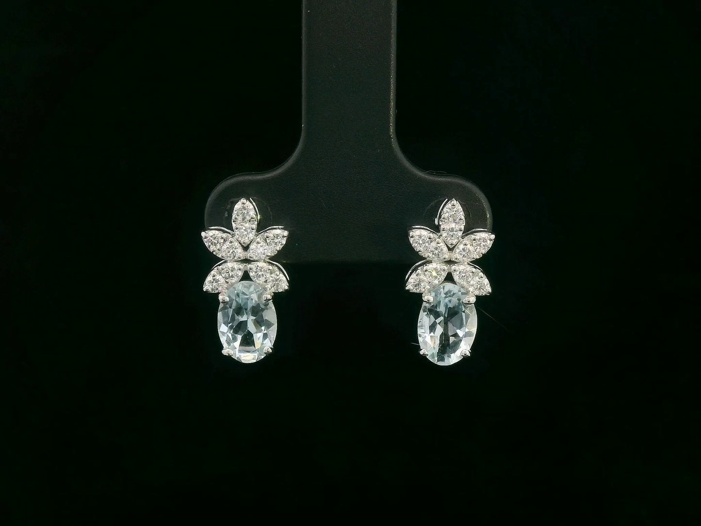 Front view of 18k gold drop earrings with oval aquamarines and floral diamond cluster