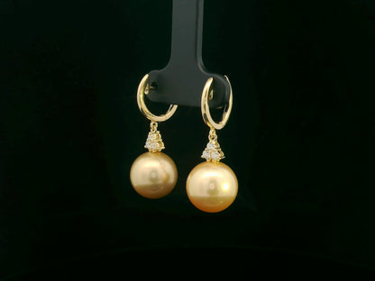 18k yellow gold South Sea pearl earrings featuring golden pearls suspended from hoops with diamond pyramid clusters above each pearl.