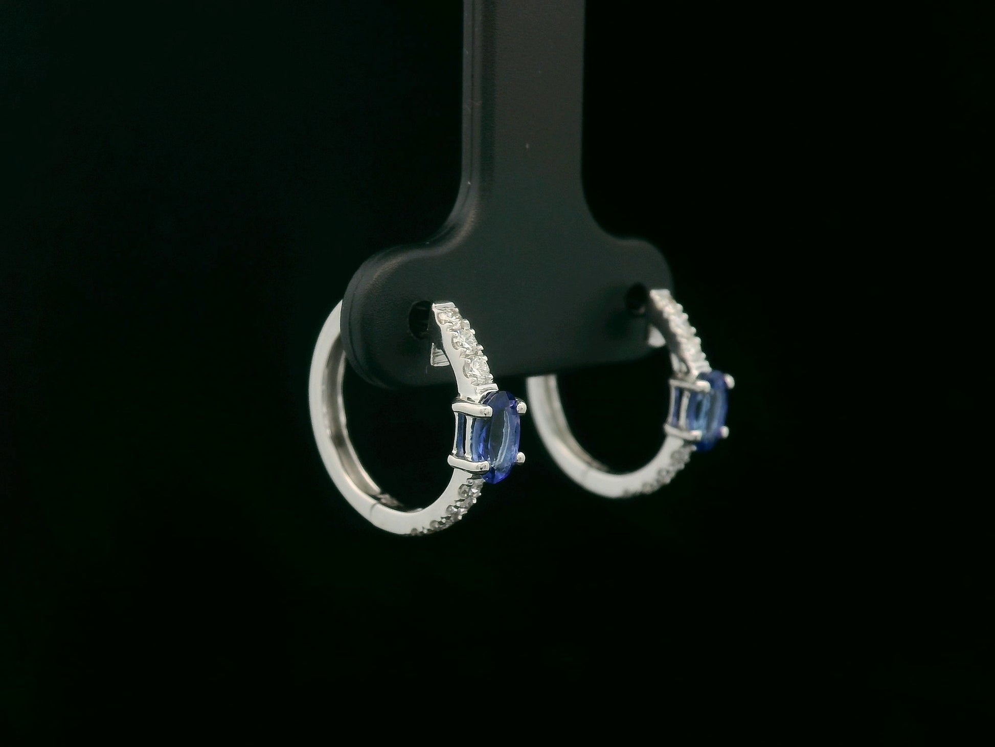 18K white gold hoop earrings featuring 0.44ct oval-cut tanzanites with 0.19ct pavé diamonds along the front curve of each hoop.