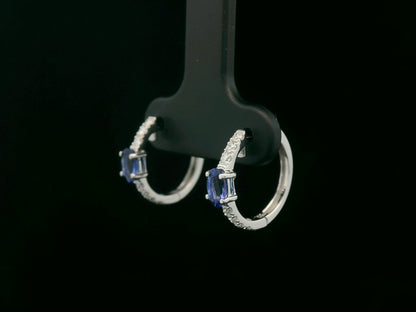 18K white gold hoop earrings featuring 0.44ct oval-cut tanzanites with 0.19ct pavé diamonds along the front curve of each hoop.