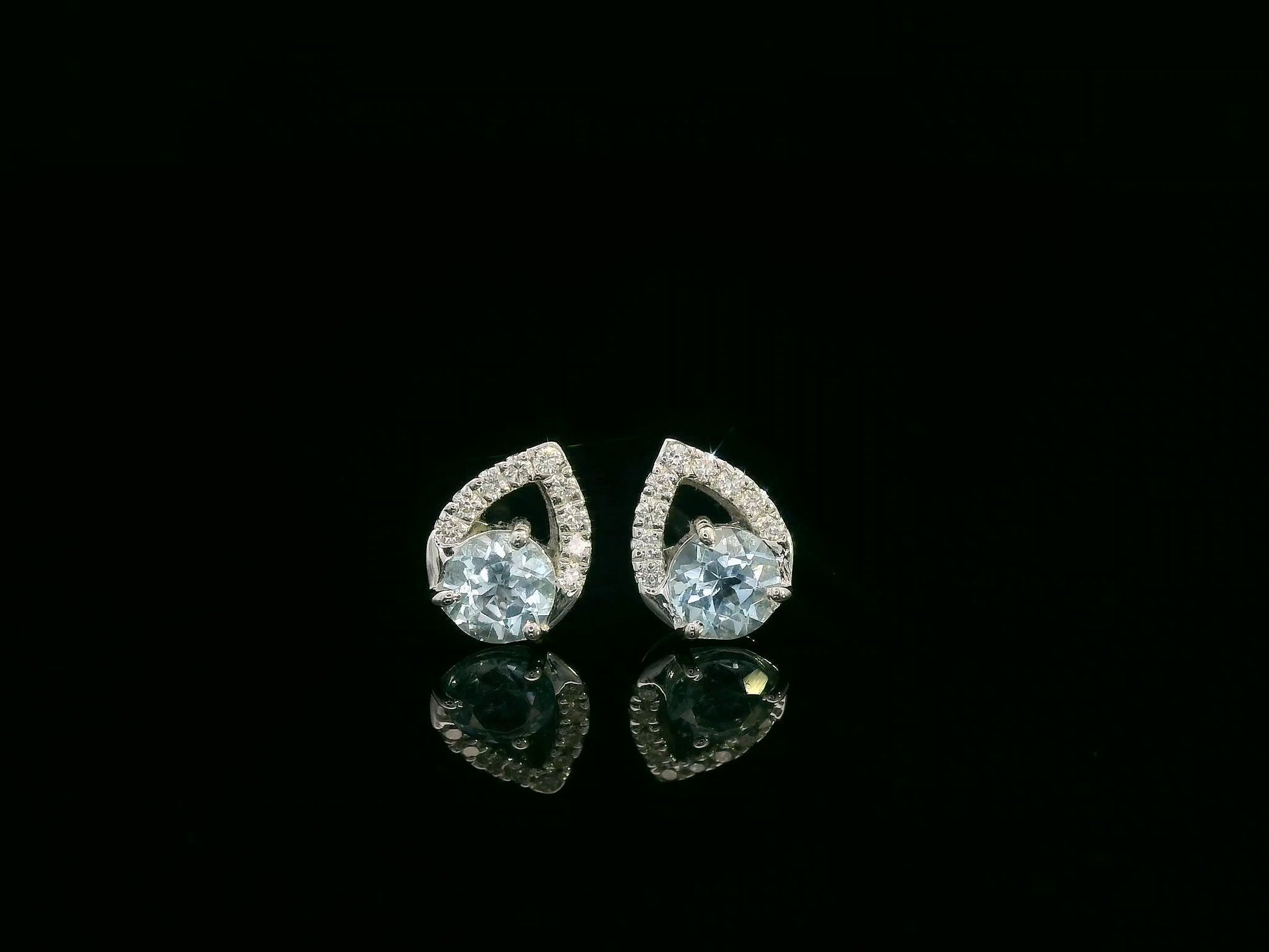 18K white gold earrings featuring 0.49ct round-cut aquamarine with 0.08ct diamond teardrop accent on one side of each stone.