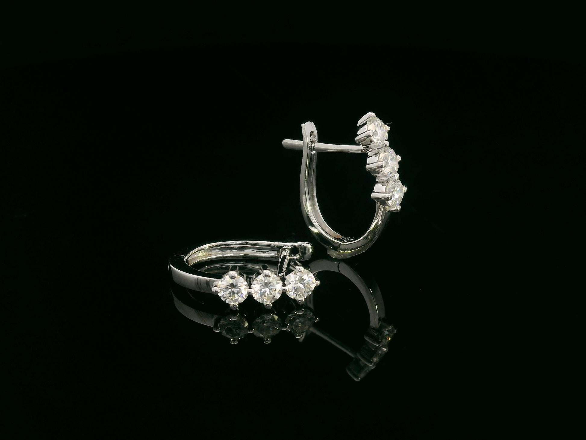 18K white gold huggie hoop earrings featuring three round brilliant-cut diamonds along the front, totaling 0.57 carat.