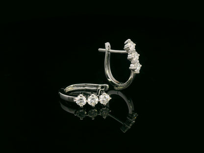 18K white gold huggie hoop earrings featuring three round brilliant-cut diamonds along the front, totaling 0.57 carat.