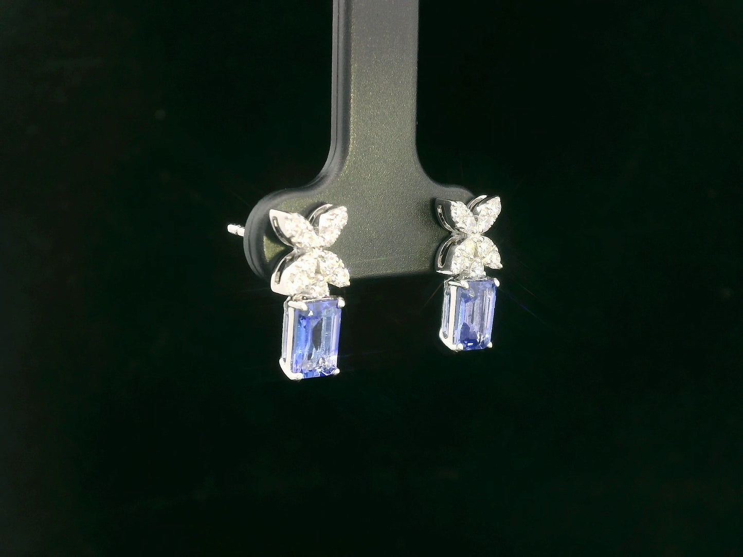 18K white gold earrings featuring emerald-cut Tanzanites beneath floral diamond clusters, total 1.56 carat
